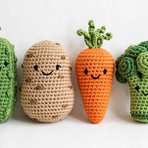 May include: A set of four crocheted vegetable toys including a green textured pickle, a tan potato with brown spots, an orange carrot with green leafy tops, and a green broccoli floret, each featuring a simple black embroidered smiling face.