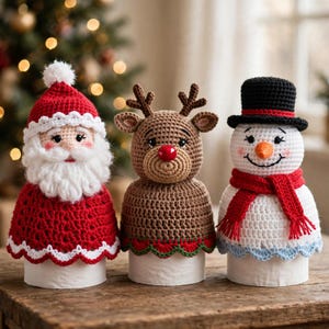 May include: Three crocheted holiday covers for toilet paper rolls featuring a Santa Claus with a red hat and white beard, a brown reindeer with a red nose and antlers, and a white snowman wearing a black top hat and red scarf.