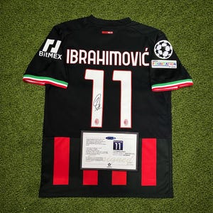 May include: Black soccer jersey with the name "IBRAHIMOVIC" and the number "11" in white. The jersey has red and green accents on the sleeves and a BitMEX logo. A signed certificate is displayed below the number.