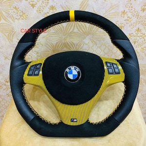 May include: Black and yellow BMW steering wheel with yellow stitching. The wheel has a perforated leather grip, yellow carbon fibre accents, and the BMW logo in the centre. The text "CAR STYLE" is visible on the top left.