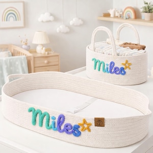 May include: An oval-shaped white woven rope changing basket and a matching round storage basket. Both feature the name Miles in a gradient green-to-blue yarn script with a yellow yarn star. The changing basket includes a white pad and strap.