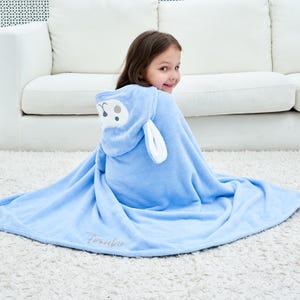 May include: A light blue hooded towel with a sheep face design. The towel has a hood with white ears and a sheep face. The towel is wrapped around a person and has the word "Frankie" embroidered on it.