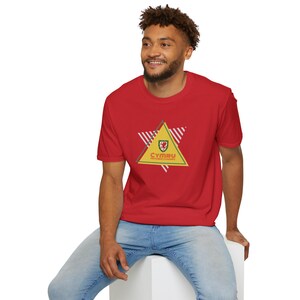 May include: Red t-shirt featuring a yellow triangle with the word "CYMRU" and a Welsh flag emblem. The shirt has a crew neck and short sleeves. The design includes white and red stripes.
