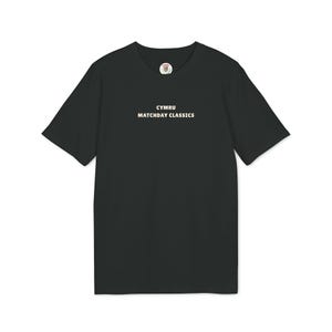 May include: Black t-shirt featuring the text "CYMRU MATCHDAY CLASSICS" in white. The shirt has a crew neck and short sleeves. A small circular emblem is at the top center of the shirt.