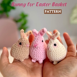 May include: Three crocheted bunny figures in tan, pink, and white, held in cupped hands. The bunnies have small black eyes and pink noses. The text "Bunny for Easter Basket" and "PATTERN" are visible in the image.