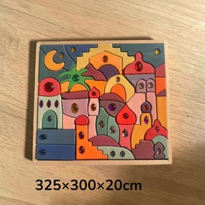 May include: A square wooden puzzle featuring a colorful city scene with various architectural shapes, domes, and a crescent moon. The puzzle pieces are decorated with embedded multi-colored faceted gems and measure 325 by 300 by 20 inches.