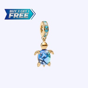May include: A gold-colored charm in the shape of a turtle with a blue and turquoise shell. The charm has a loop at the top with turquoise-colored stones. The image also includes the text "BUY 2 GET 1 FREE" in a blue banner.