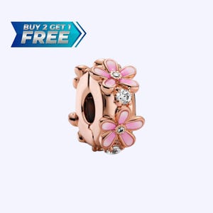 May include: Rose gold charm with pink enamel flowers and clear crystal accents. The charm features a floral design with a central hole for threading onto a bracelet or necklace. The text "BUY 2 GET 1 FREE" is in the upper left corner.
