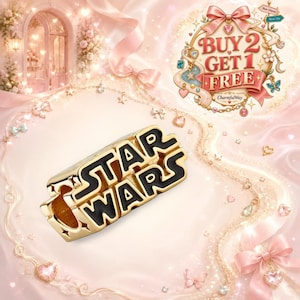 May include: A gold-toned metal charm featuring the Star Wars logo in black enamel lettering. The charm has a rectangular shape with star-shaped cutouts at the corners. The text STAR WARS is clearly visible in the iconic font style on the front surface.