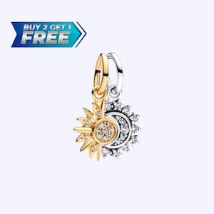 May include: A gold and silver charm pendant featuring a sun and moon design. The sun side is gold with a central circle and surrounding rays, both adorned with clear crystals. The moon side is silver with crystal accents. The text "BUY 2 GET 1 FREE" is in the upper left.