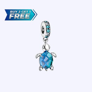May include: A silver charm with a blue and turquoise sea turtle design. The turtle has a patterned shell and is suspended from a ring adorned with blue and clear stones. Text in the image reads "BUY 2 GET 1 FREE."