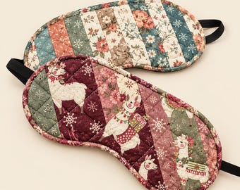 May include: Two quilted sleep masks with elastic straps. The top mask features vertical stripes of floral patterns in teal, cream, and coral. The bottom mask displays a diagonal patchwork design with white llamas, snowflakes, and floral motifs in burgundy.