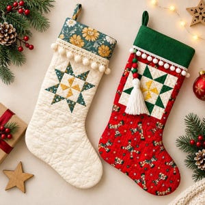 以下が含まれることがあります： キルティング加工された2つのクリスマスストッキング。左側はクリーム色で花柄の袖口と緑と黄色の星型キルトブロック付き。右側は赤色でくるみ割り人形のプリント、緑色の袖口、星型キルトブロック、白いタッセルが付いています。