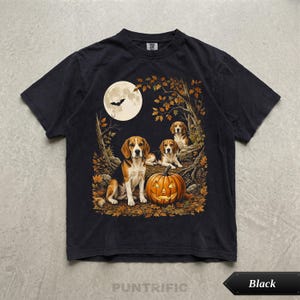 May include: A black short-sleeved t-shirt featuring a graphic print of three beagle dogs sitting in an autumn forest with a carved jack-o'-lantern pumpkin, a full moon, and a flying bat silhouette against a backdrop of fallen orange leaves.
