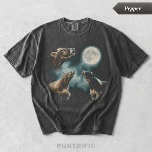 Puede incluir: Una camiseta de manga corta gris carbón con acabado de lavado vintage. El estampado gráfico muestra tres vacas mirando hacia una luna llena sobre un cielo nocturno oscuro y nublado. La camiseta tiene cuello redondo y un corte estándar.