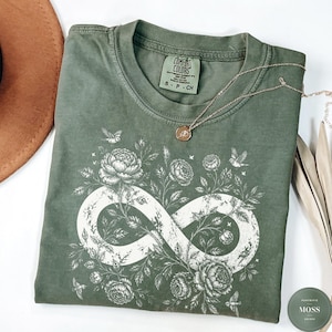 May include: An olive green t-shirt featuring a white infinity symbol graphic intertwined with detailed floral illustrations of roses and small birds. The shirt has a crew neckline and a Comfort Colors brand label printed on the inside collar.