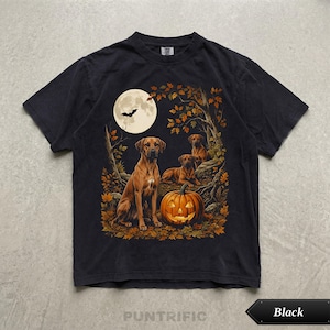 May include: A black short-sleeve t-shirt featuring a graphic print of three brown dogs in an autumn forest setting. The scene includes a large glowing jack-o'-lantern, a full moon with a flying bat silhouette, and orange fall foliage.