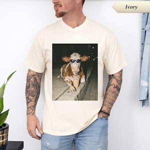 Cream t-shirt with a cow wearing sunglasses holding a coffee.