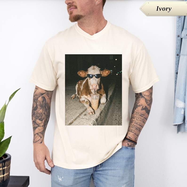 Cream t-shirt with a cow wearing sunglasses holding a coffee.