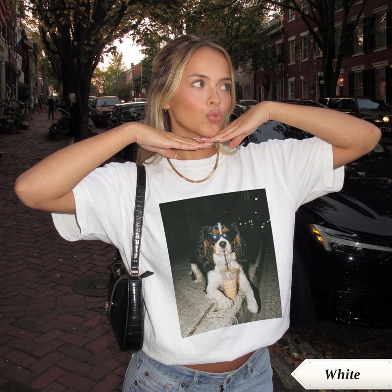 Woman in white t-shirt with dog photo, holding a coffee.