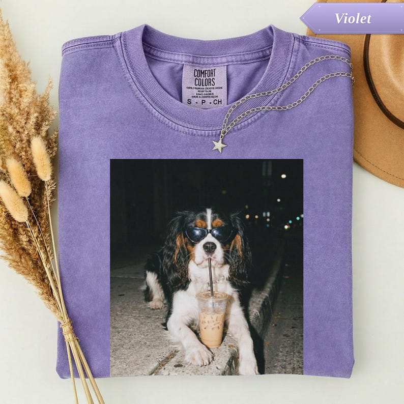 Dog wearing sunglasses sips a drink on a t-shirt with a star necklace.