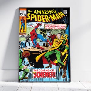 May include: Framed vintage comic book cover of The Amazing Spider-Man. The cover features Spider-Man in action, battling a villain in a yellow cape. Bold text reads "The Amazing Spider-Man" and "The Coming of the Schemer!" The comic is in a black frame.