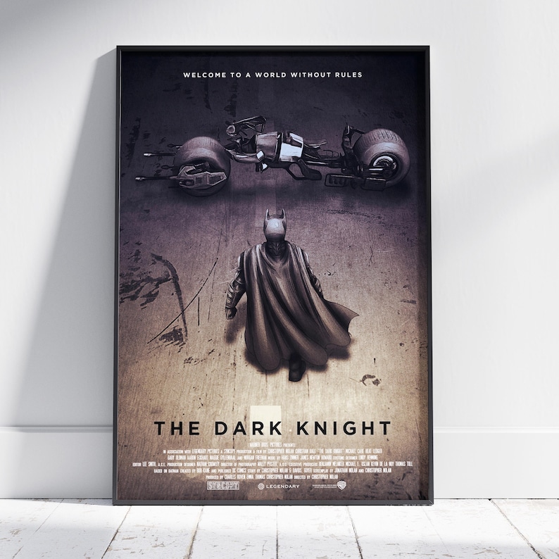 May include: A framed movie poster for The Dark Knight featuring a dark, textured background. The top text reads WELCOME TO A WORLD WITHOUT RULES. Below, a caped figure stands before a futuristic motorcycle. The title THE DARK KNIGHT is centred.