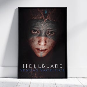 Puede incluir: Póster enmarcado con un primer plano de un rostro con marcas tribales y una corona. El póster tiene el texto "HELLBLADE SENUA'S SACRIFICE" en blanco y azul. La imagen está sobre un fondo oscuro.