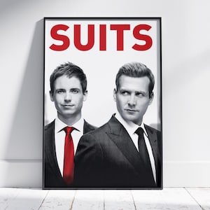 May include: A framed poster featuring two men in suits. The word "SUITS" is displayed in large, red letters at the top. One man wears a red tie, the other a black tie. The background is white.