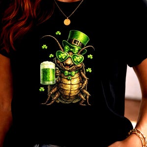 May include: Black t-shirt featuring a St. Patrick's Day themed insect character. The insect wears a green hat, heart-shaped glasses, and a bow tie, holding a green beer. Shamrock accents complete the design.