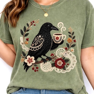 Black crow holding a coffee cup with floral and lace details on a green Comfort Colors t-shirt