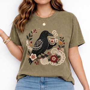 Black crow holding a coffee cup with floral and lace details on a khaki Comfort Colors t-shirt