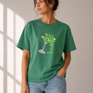 Green t-shirt featuring a rhinestone martini glass filled with green shamrocks. The shamrocks cascade from the glass. The shirt is a solid green color and has a relaxed fit.