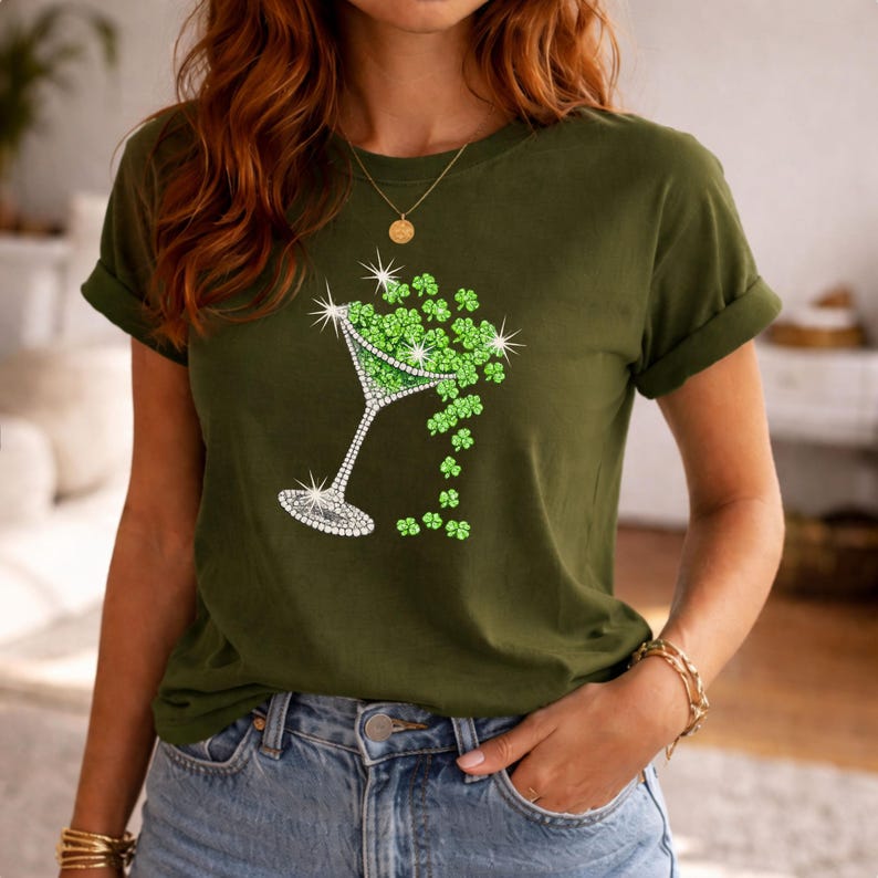 Olive green t-shirt featuring a rhinestone martini glass filled with green shamrocks. The glass design has a sparkling rim and stem. The shamrocks are spilling out of the glass. The shirt is a casual style.