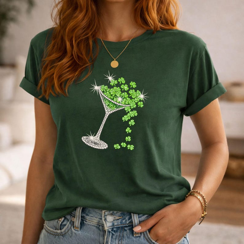 Dark green t-shirt featuring a martini glass design filled with green shamrocks. The martini glass is outlined with sparkling rhinestones. The shirt has rolled-up sleeves and a round neckline.