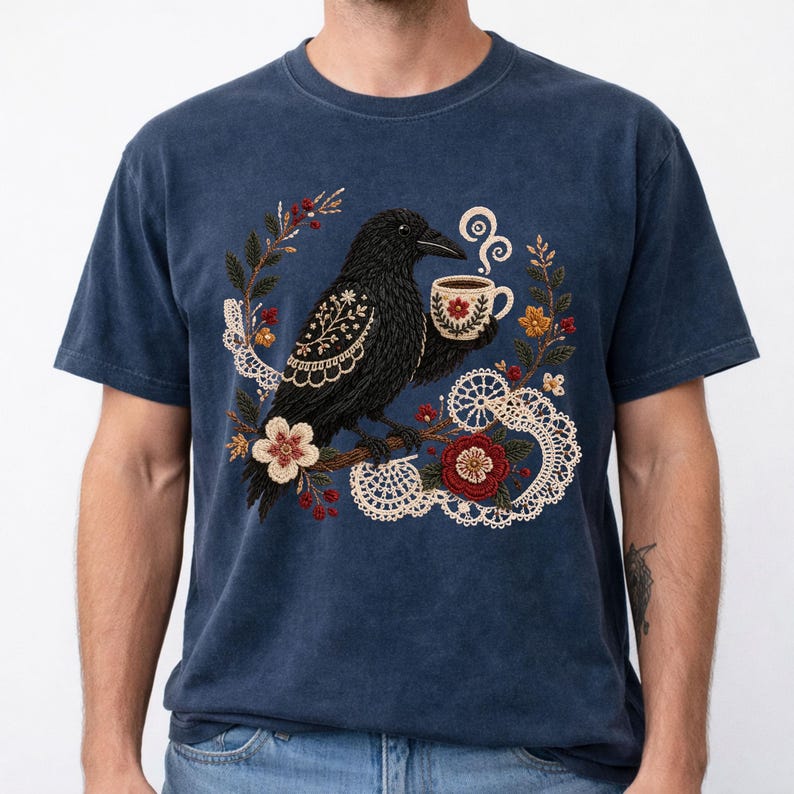 Black crow holding a coffee cup with floral and lace details on a navy Comfort Colors t-shirt