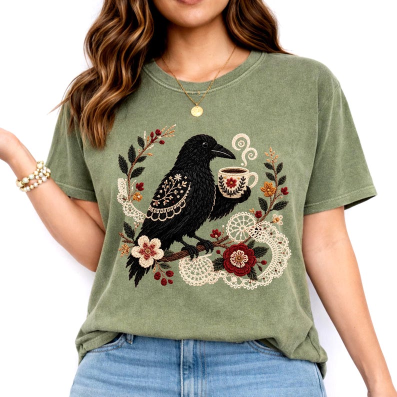 Black crow holding a coffee cup with floral and lace details on a green Comfort Colors t-shirt