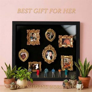 Może przedstawiać: Czarna oprawiona ekspozycja z kilkoma złotymi, ozdobnymi ramkami do zdjęć o różnych kształtach, każda z fotografią. Miniaturowe figurki znajdują się pod ramkami. Tekst "BEST GIFT FOR HER" znajduje się na górze.
