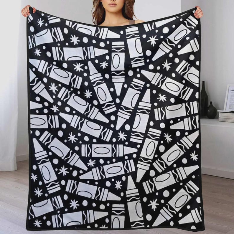 K&ouml;nnte beinhalten: Eine rechteckige Decke mit einem sich wiederholenden schwarz-wei&szlig;en Muster aus Wachsmalstiften und kleinen Sternformen. Das Design ist in verschiedene Richtungen &uuml;ber die gesamte Stoffoberfl&auml;che verteilt und erzeugt einen kontrastreichen Druck.