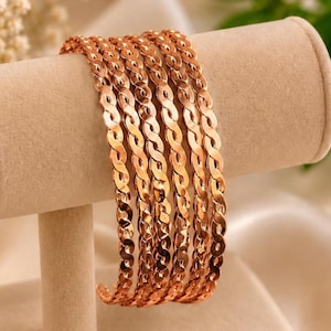 May include: A set of five rose gold-toned bangles, each featuring a continuous, interlocking twisted chain link design. The bracelets have a polished, reflective metallic finish and are arranged side-by-side in a uniform, circular formation.
