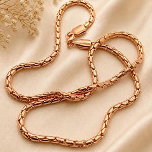 May include: A rose gold-toned chain necklace featuring a series of interconnected, rounded, pill-shaped links. The chain has a polished, metallic finish and includes a secure lobster claw clasp mechanism at the end for fastening the necklace.
