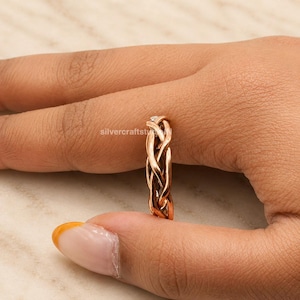 May include: A copper-toned ring featuring a braided or woven metal design. The band consists of multiple intertwined strands that create a textured, openwork pattern around the circumference of the ring. The metal has a warm, reddish-brown finish.