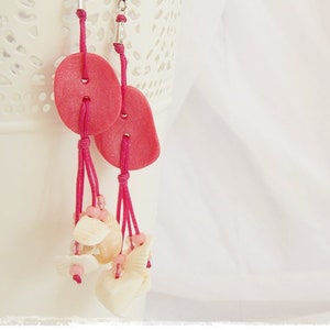 Può includere: Orecchini a bottone rosa con dettagli floreali bianchi appesi su uno sfondo di pizzo bianco.