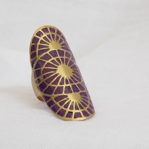 Peut inclure: Une bague en or avec un motif en émail violet représentant trois cercles qui se chevauchent avec un motif géométrique.