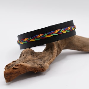 Puede incluir: Pulsera de cuero negro con un cordón trenzado arcoíris.