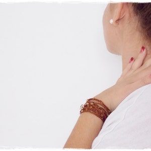 Op de afbeelding: Een vrouw draagt een wit shirt met een bruine kralen armband om haar pols. Haar nagels zijn rood gelakt.