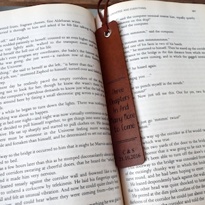 May include: A brown leather bookmark with the text "Three Chapters In And Many More To Come" and the date "C&S 21.10.2016" engraved on it. The bookmark is placed on an open book.