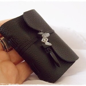 May include: A small black leather journal with a silver clasp and a black tassel. The journal is closed and has a textured surface.