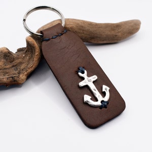 Könnte beinhalten: Brauner Leder-Schlüsselanhänger mit einem silbernen Anker-Anhänger und blauen Nähten.
