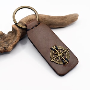 May include: Brown leather keychain with a brass compass charm. The compass has the letters N, S, E, and W around the edge.